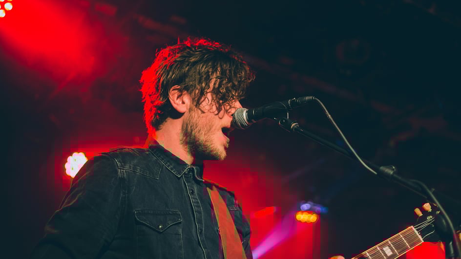 A man plays guitar while singing against a red backdrop, creating one of Soundstripe’s most popular royalty free songs of 2024.