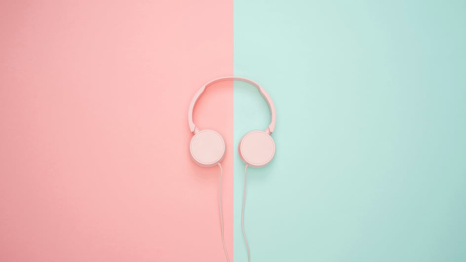  A pair of pink headphones sits on a pink and turquoise background, playing royalty free Adobe Express music.