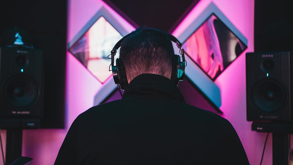  A man wears headphones and sits between 2 speakers, listening to 8d surround sound.