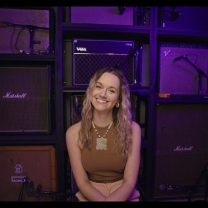 Soundstripe artist Ashton Myers sits in front of a wall of music amps, reflecting on working with music licensing companies.