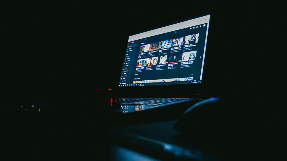  A laptop sits on a desk in a dark room with YouTube showing on the screen. The user is trying to figure out how to add text to YouTube videos.